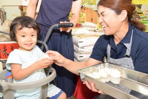Aコープを訪れた子供におにぎりを手渡す生産者の女性