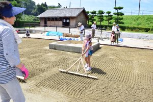 海水をまいた塩田の砂に筋を付ける参加者の子供ら